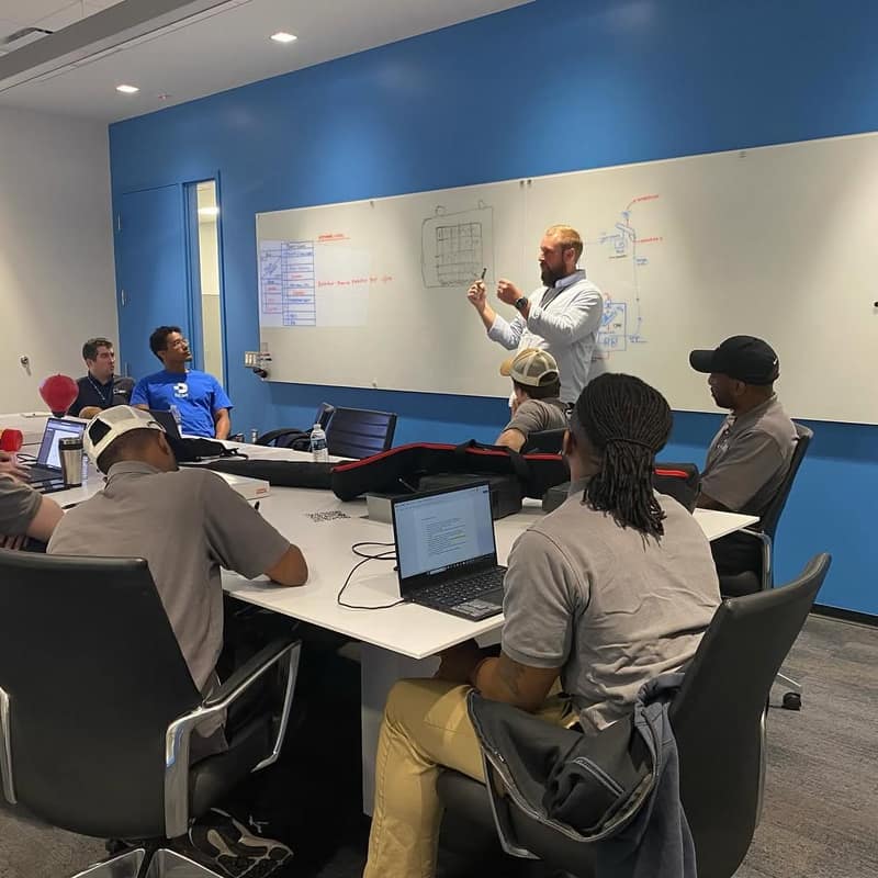 Instructor at a whiteboard leading a training session for a room of technicians
