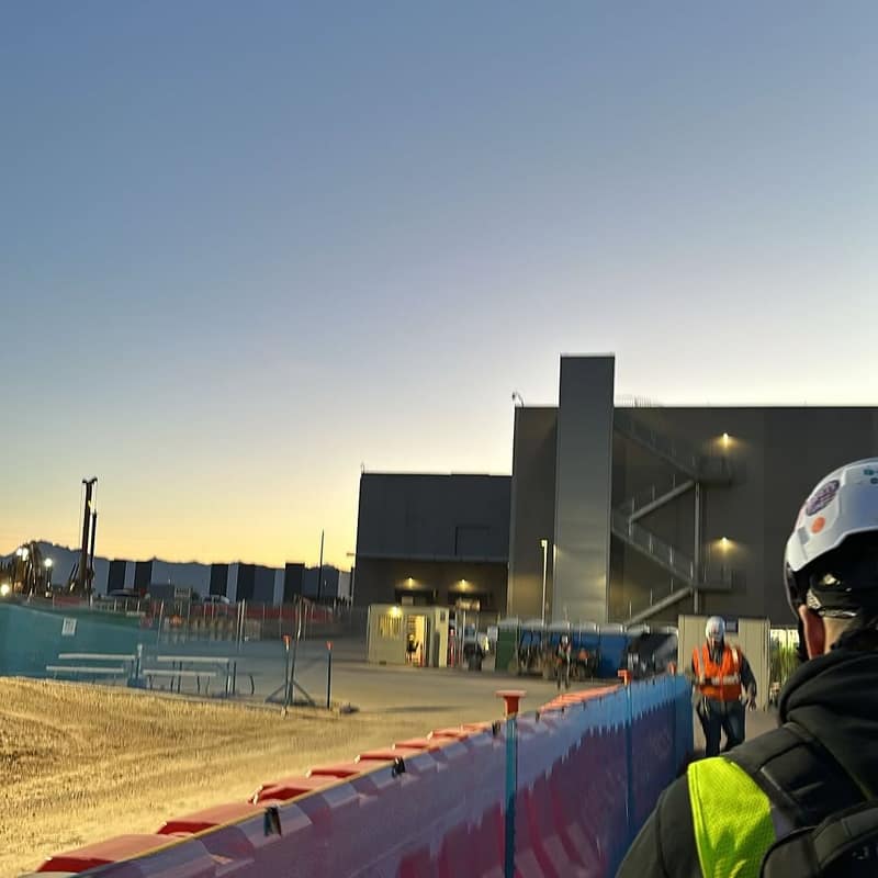 Crew in hard hats and high-visibility vests arriving at a data center construction site at sunrise